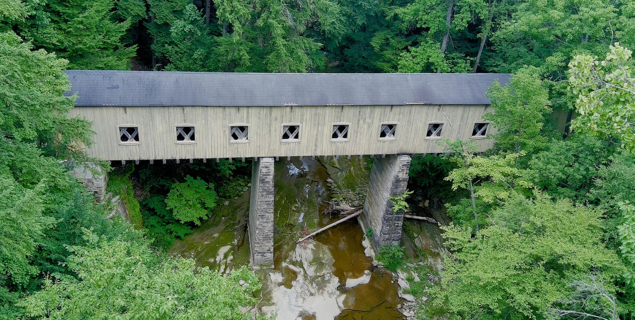 Aerial view of Windsor Mills covered bridge spanning a wooded creek